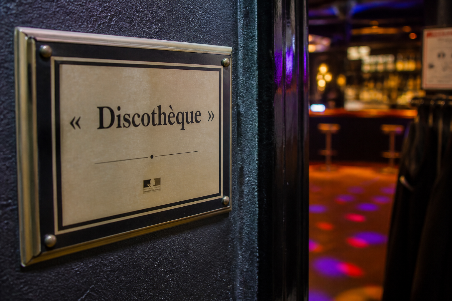 Gros plan sur une signalétique de discothèque avec arrière-plan flou de bar et ambiance nocturne d’établissement lillois.