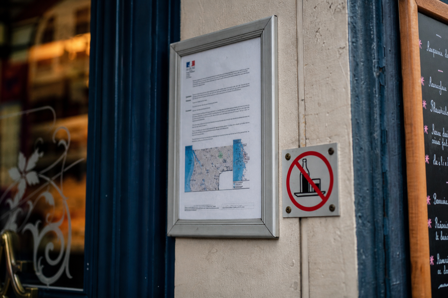Gros plan sur des affichages réglementaires à l’entrée d’un restaurant du centre-ville, avec ambiance de nuit en arrière-plan.