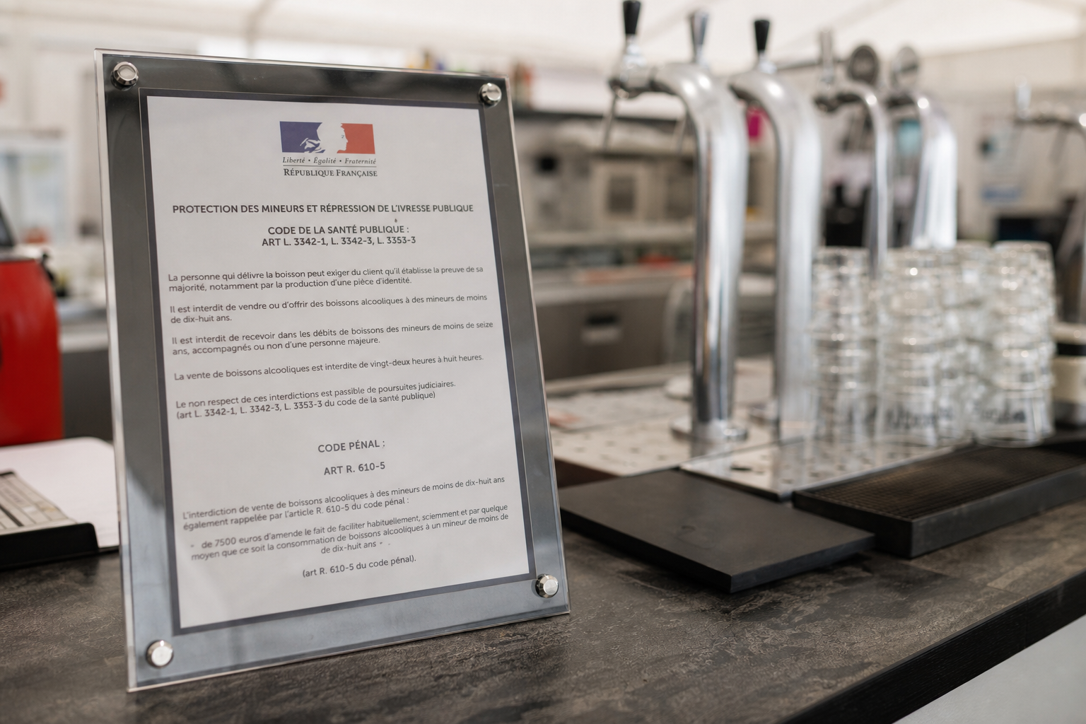Gros plan sur un affichage réglementaire près d’un comptoir de bar dans l’enceinte d’un circuit, avec verrerie en arrière-plan.